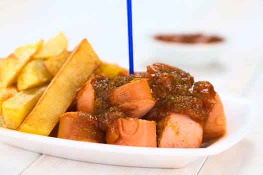 German fast food called Currywurst served with French fries on a disposable plate with plastic party fork (Selective Focus, Focus on the front of the sausage on top) 