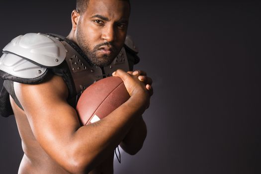 A young male football player athlete holds ball wearing shoulder pads