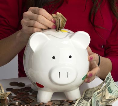 Female hand fills Piggy Bank with American Cash Currency