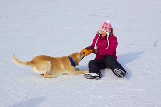 Happy attractive girl with ice skates playing with her dog on frozen lake
