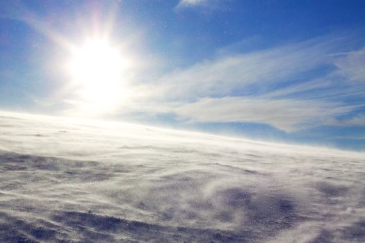 Winter scenery with sun and wind blowing snow