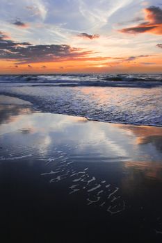 Colorful cloudy sunset at the beach with reflection - vertical