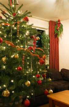 Living room with warm lighted decorated christmas tree in december - vertical