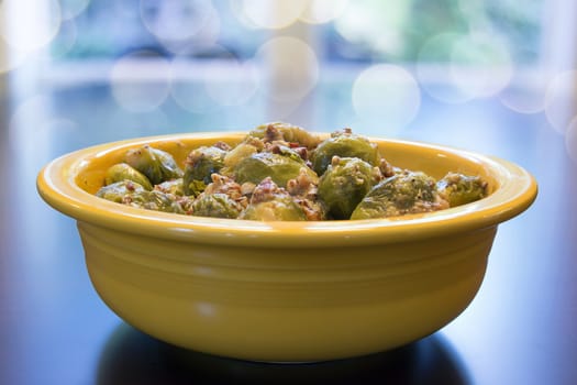 Brussel Sprouts Cooked with Pancetta Olive Oil and Onions in Yellow Bowl with Bokeh Blurred Background
