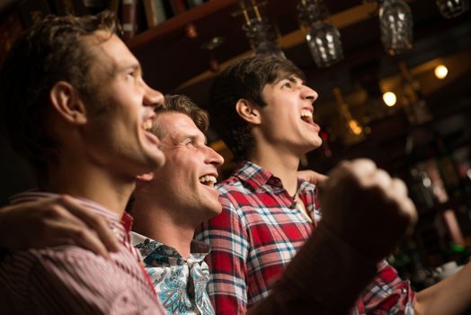 Three men stand in a row embracing smile and look in front of you, sports fans