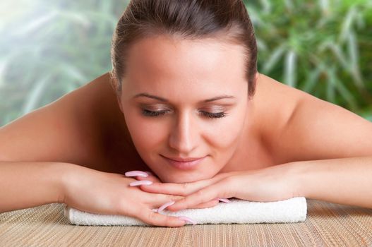 Young woman lying in a spa ready to get a massage in a green background