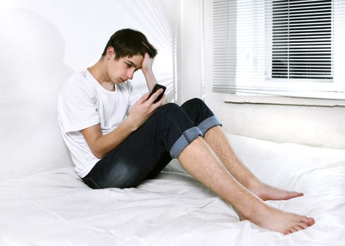 Sad Young Man with Cellphone sitting on the bed