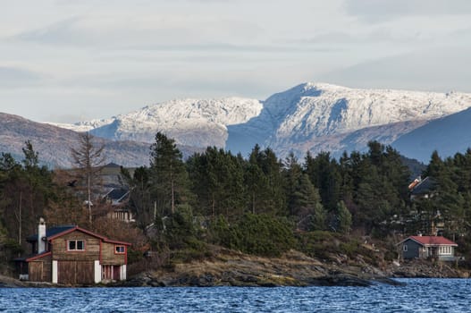 Cabins by the coast with mountains covered in snow in the background