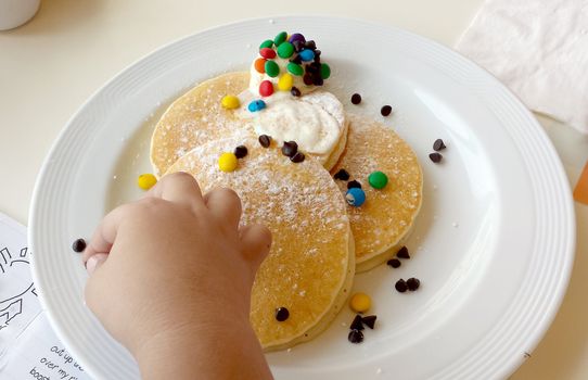 little hand picking a chocolate chip off a plate full of pancakes