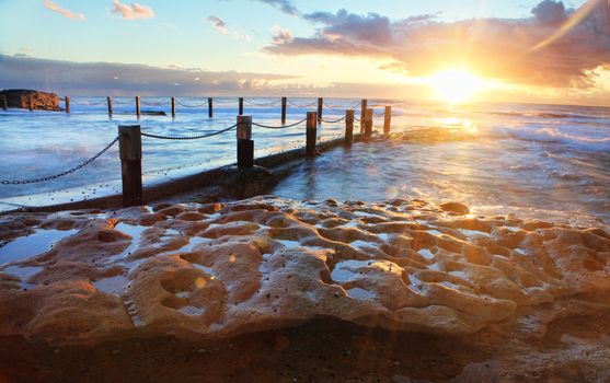 Golden rays of sunlight emerge at sunrise at the idyllic Mahon pool located on exposed rock shelf at Maroubra, Sydney Australia