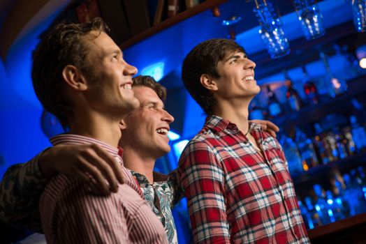 Three men stand in a row embracing smile and look in front of you, sports fans