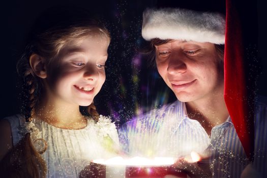 father in Santa Claus cap and daughter opened a box with Christmas gift boxes of shining light and magic