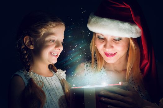 mother in Santa Claus cap and daughter opened a box with Christmas gift boxes of shining light and magic