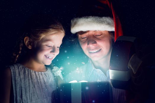 father in Santa Claus cap and daughter opened a box with Christmas gift boxes of shining light and magic