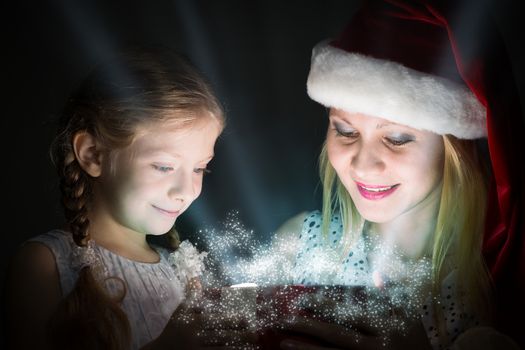 mother in Santa Claus cap and daughter opened a box with Christmas gift boxes of shining light and magic