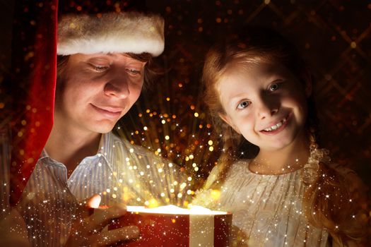 father in Santa Claus cap and daughter opened a box with Christmas gift boxes of shining light and magic