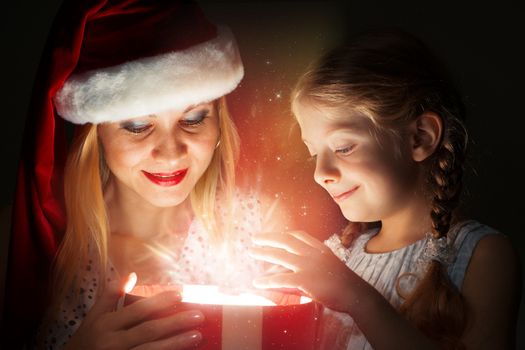 mother in Santa Claus cap and daughter opened a box with Christmas gift boxes of shining light and magic