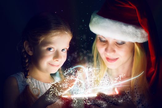 mother in Santa Claus cap and daughter opened a box with Christmas gift boxes of shining light and magic