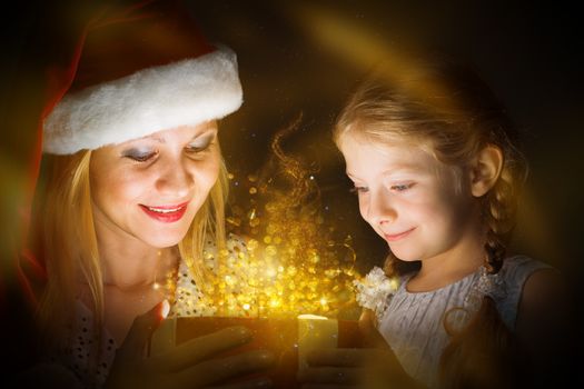 mother in Santa Claus cap and daughter opened a box with Christmas gift boxes of shining light and magic