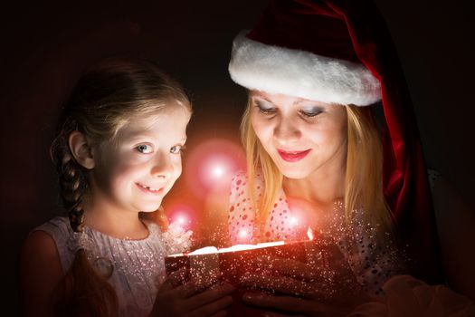 mother in Santa Claus cap and daughter opened a box with Christmas gift boxes of shining light and magic