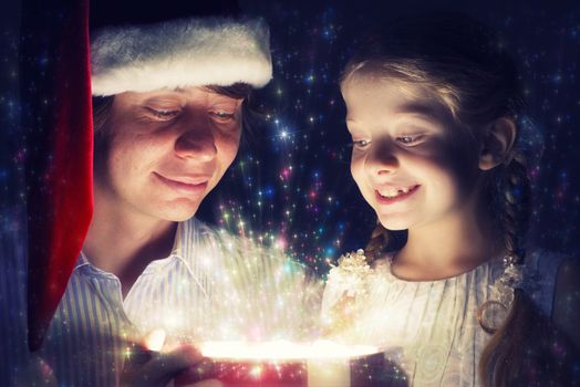 father in Santa Claus cap and daughter opened a box with Christmas gift boxes of shining light and magic