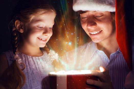 father in Santa Claus cap and daughter opened a box with Christmas gift boxes of shining light and magic