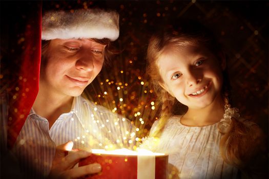 father in Santa Claus cap and daughter opened a box with Christmas gift boxes of shining light and magic