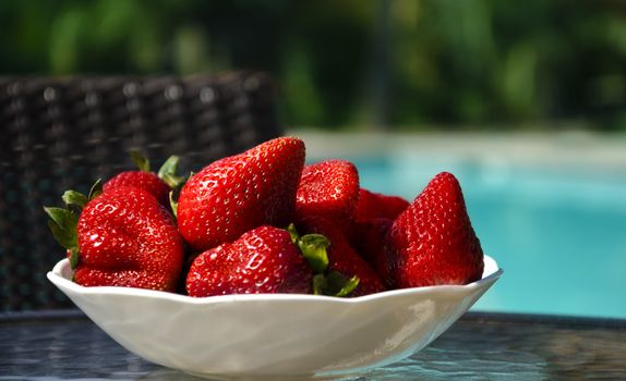 Strawberry in white plate on table by the swimming pool