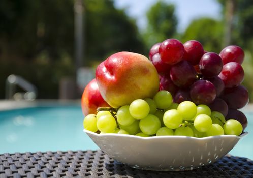 Two peaches and grape in white plate on table by the swimming pool