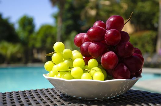 Grape in white plate on table by the swimming pool