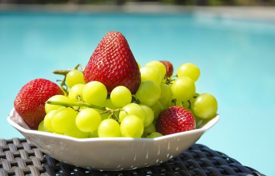 Strawberry and grape in white plate on table by the swimming pool