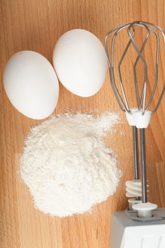 Two eggs and flour and mixer on a wooden table ready to baking