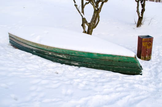 old wooden boat lying upside down snow bank near the shore in winter time