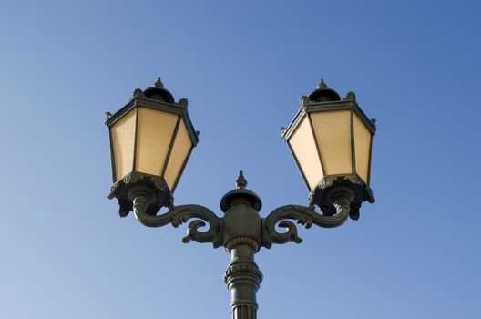 vintage iron lighting pole with twin double lamp lantern on background of dark blue sky.