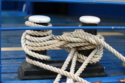 Close-up of a mooring rope with a knotted end tied around a cleat on a wooden pier/ Nautical mooring rope