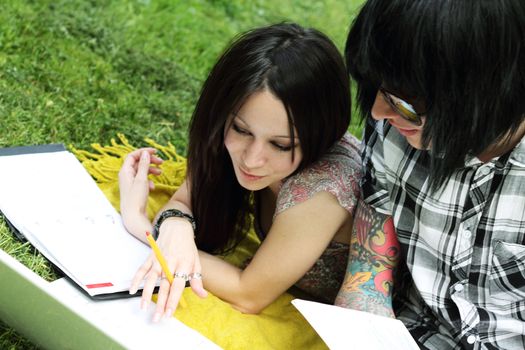 Couple of young students studying outdoors with laptop and books