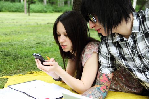 Couple of young students studying outdoors with laptop and books