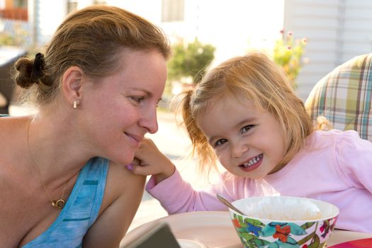 Little girl toddler touching her mothers shoulder softly while mother looks at her daughter at the table