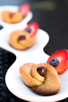 Turkish style rose sweet with hazelnut garnished with strawberries and blueberries, served on a long rounded white plate on a wicker table