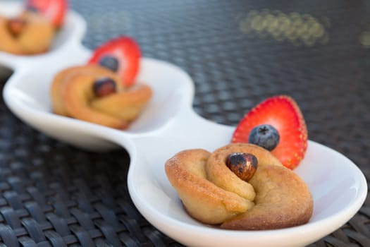 Turkish style rose sweet with hazelnut garnished with strawberries and blueberries, served on a long rounded white plate on a wicker table