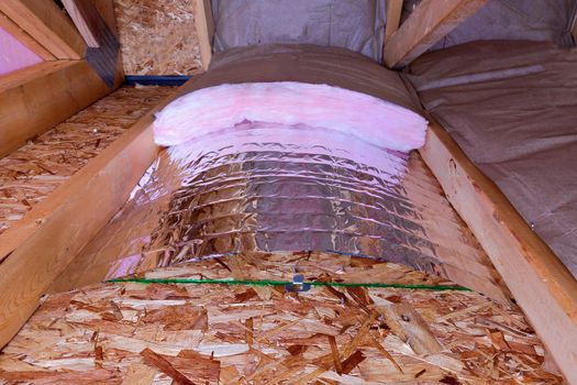 Insulatin of attic with fiberglass cold barrier and reflective heat barrier used as baffle between the attic joists, work is ongoing