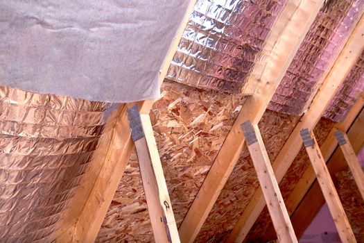 Inside gable and joist view of ongoing project, insulation of attic with fiberglass cold barrier and reflective heat barrier between the attic joists