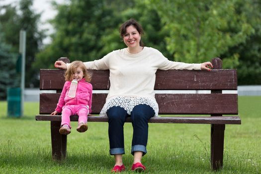 Mother and her toddler daughter having fun trustful moments outside on the bench