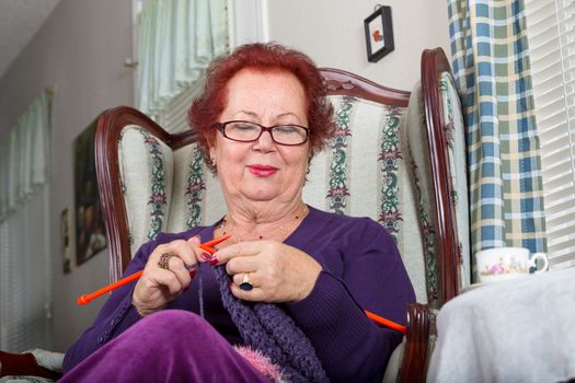 Senior woman relaxing while knitting, she sits on a fancy old classic style chair and pays attention to her crochet