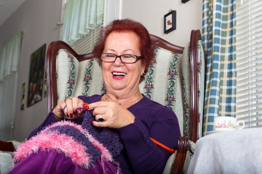 Senior happy woman laughing while knitting, she sits on a fancy old classic style chair