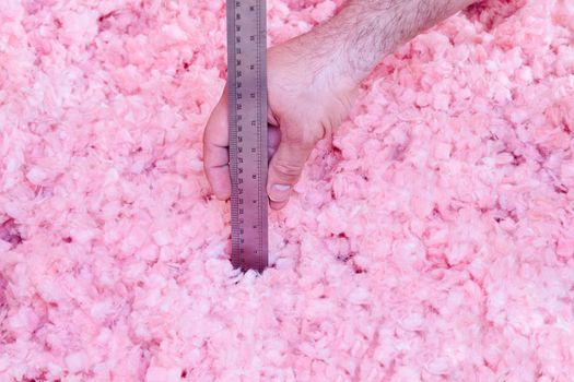 Homeowner checking the energy efficiency of their house by measuring the thickness of fiberglass insulation in the attic