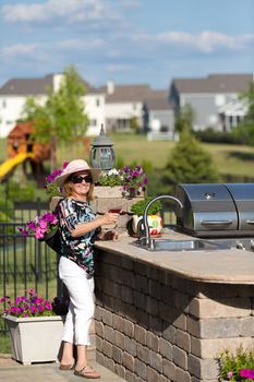 Mature blonde lady toasting her martini glass out at the patio next to the kitchen counter top