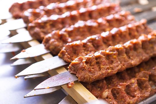 Several Adana Kebab skewers lined up waiting to be cooked and served