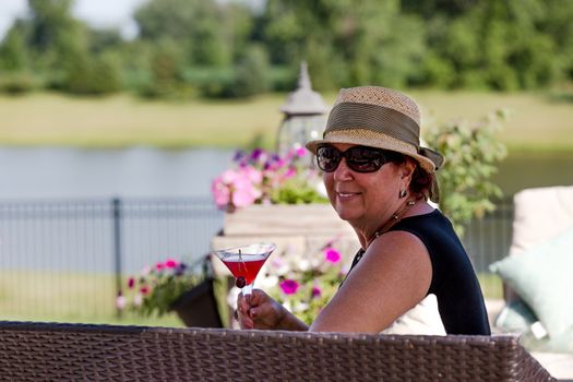 Senior lady toasting her martini glass out at the patio infront of petunias