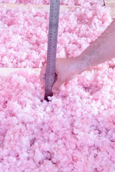 Contractor checking the energy efficiency of their house by measuring the thickness of fiberglass insulation in the attic